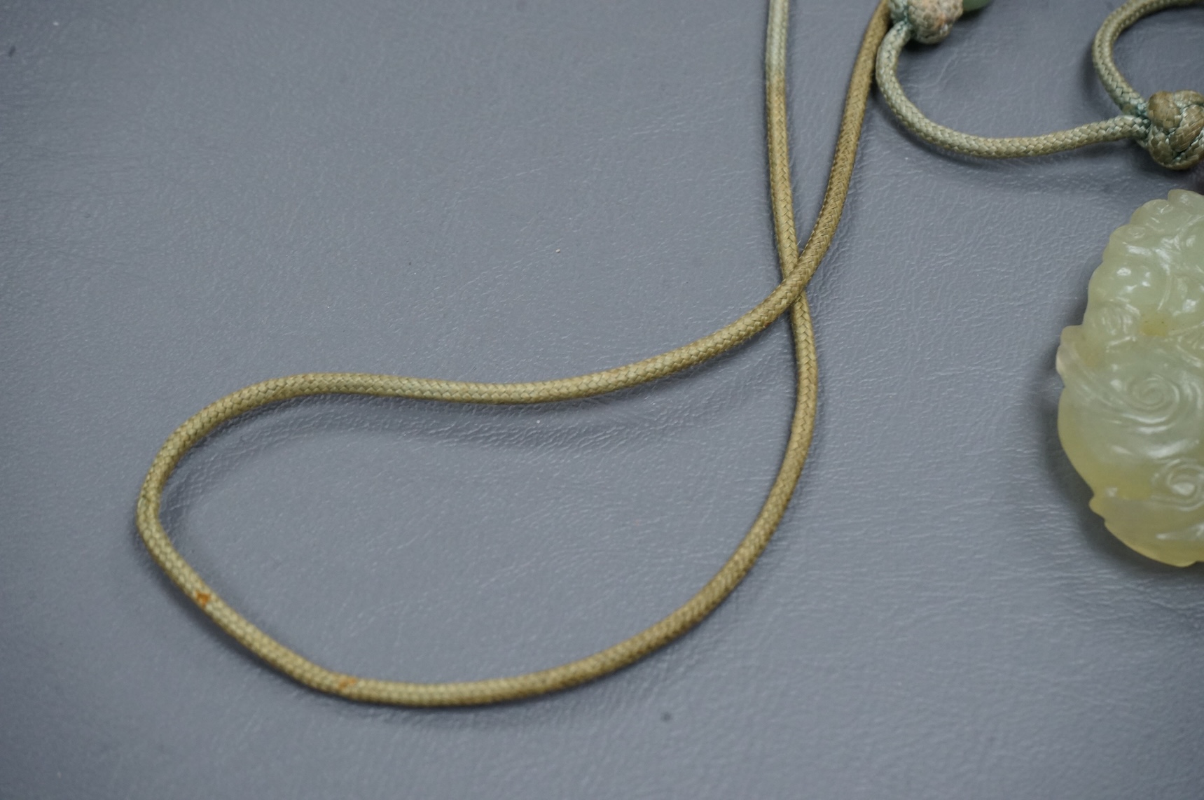 A Chinese carved bowenite jade pendant, on knotted beaded cord, pendant 6cm long.